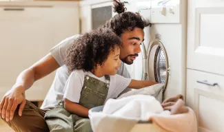 Father and child excitedly watching clothes inside a washing machine.