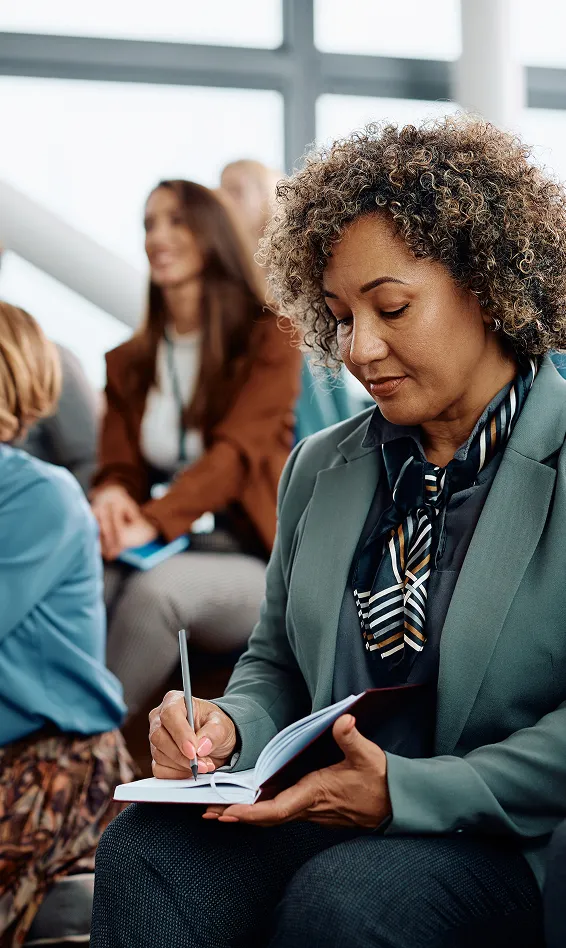 A woman attending a seminar and taking notes while listening.