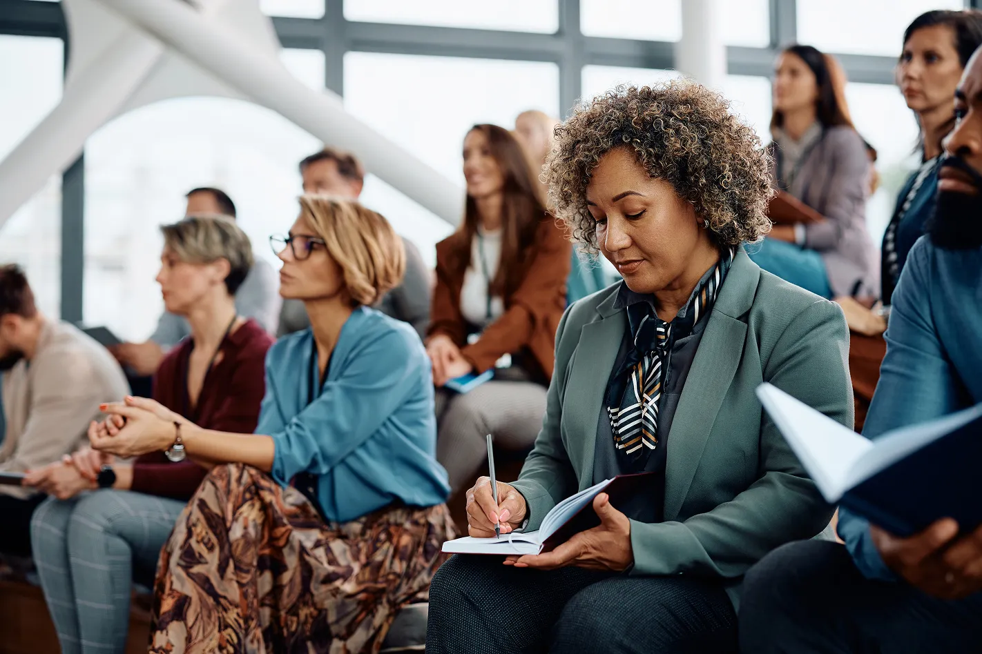 A woman attending a seminar and taking notes while listening.