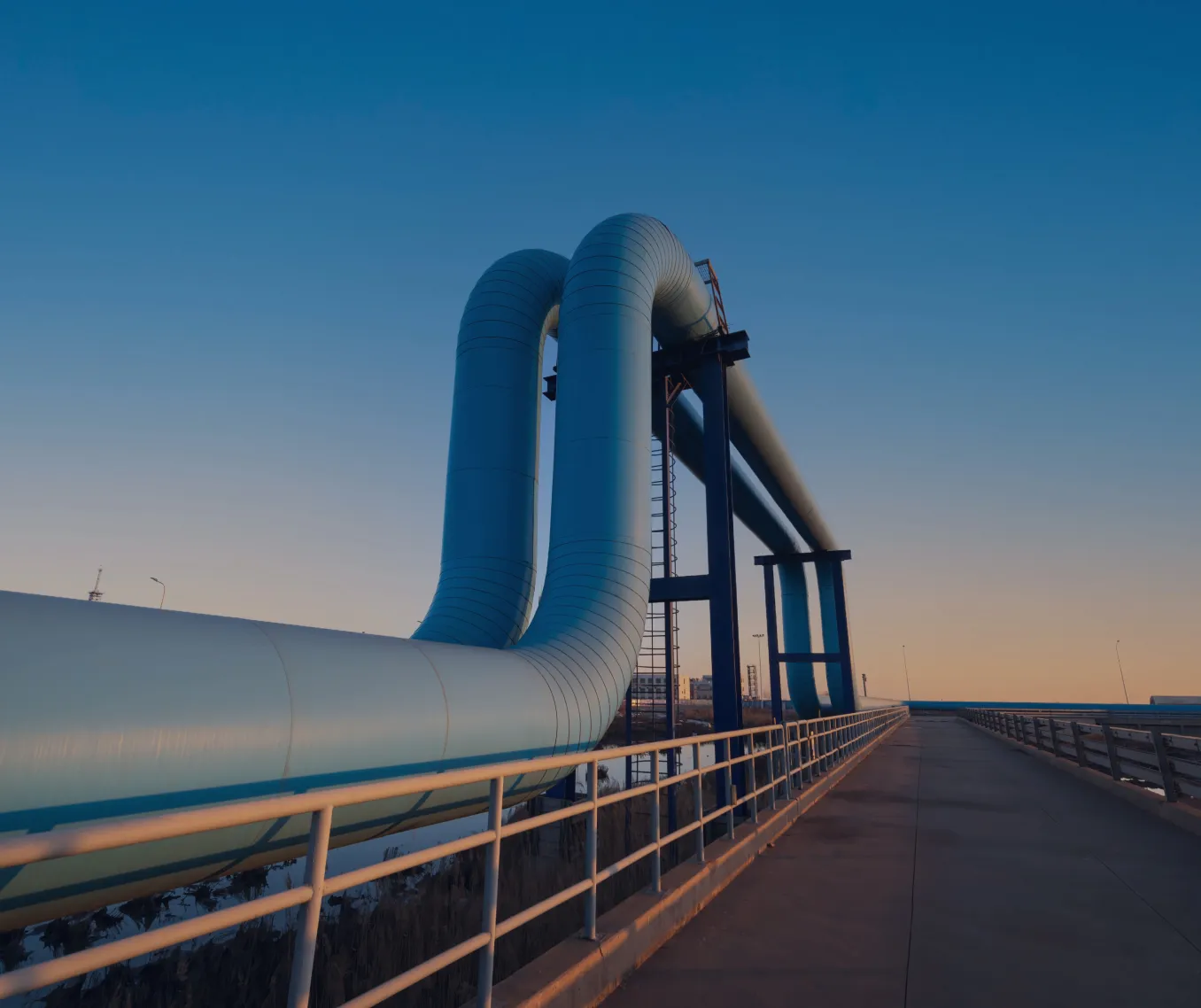 Large blue pipelines supported by a dark metal structure against a clear blue sky.