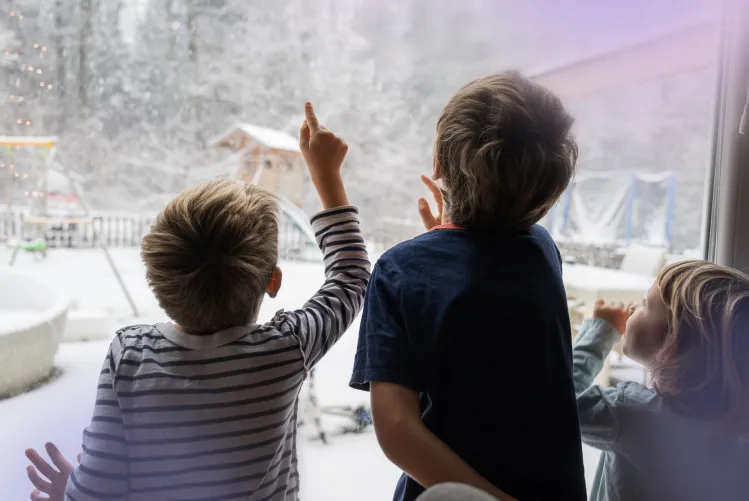 3 children looking out the window at snow.